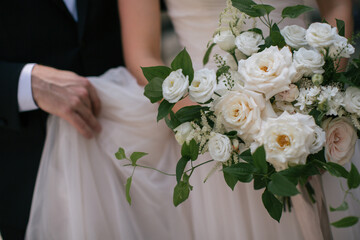 Closeup of bride holding bouquet while groom holds her dress