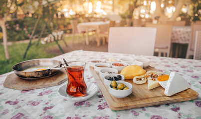Freshly prepared Turkish Breakfast consisting of scrambled eggs, tea, vegetable salad and an assortment of snacks and pickles. Beautifully set table in the outdoor restaurant in the garden
