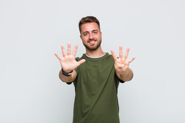 young man smiling and looking friendly, showing number nine or ninth with hand forward, counting...