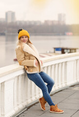  blond model girl in knitted hat and coat with maple leaf close up portrait on city architecture background