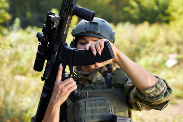 military woman is checking details of weapon before military training loading gun outdoors, sport...