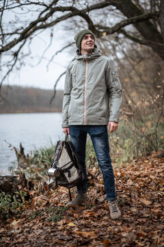 Full body photo of man holding his backpack with one hand enjoying autumn lake scenery