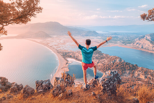 Happy fit man spread his arms while enjoying stunning view from the top of the mountain to the colorful sea bay and the coast in mediterranean resort