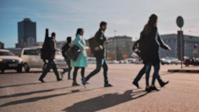 Lens blur, out of focus. A crowd of pedestrians is walking along the street with cars in the background. People walk around the big city on a sunny day. Slow motion