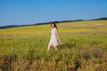 Fototapeta na wymiar Beautiful woman in dress walks on the field happily one