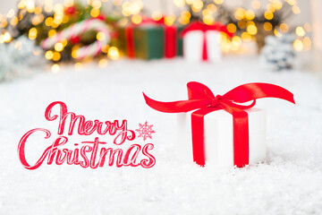 Merry Christmas lettering on the greeting card with gift boxes, lights and snow. 