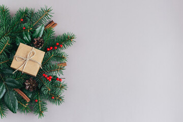 Christmas background with spruce branches, red berries, cones, cinnamon sticks and craft gift box. Holiday eco-friendly concept.