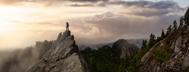 Adventurous Man on top of a rugged rocky mountain. Dramatic Colorful Sunrise Sky Art Render. Taken on Crown Mountain, North Vancouver, BC, Canada.