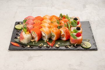 Big beautiful set of different types of sushi maki on a black rectangular stone slate plate. A traditional Japanese dish of raw fish and seafood wrapped in boiled rice and nori seaweed.