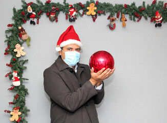latin man with protection mask, santa claus hat and red sphere,
Christmas decoration, new normal...