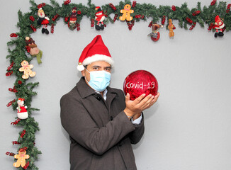latin man with protection mask, santa claus hat and red sphere,
Christmas decoration, new normal...