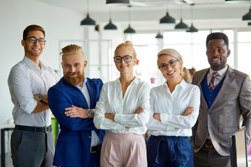 portrait of successful multi-ethnic team looking at camera in the office, posing, young people have a good cooperation, stand with crossed hands smiling