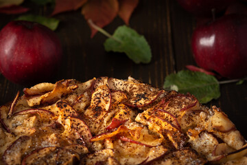 Delicious sweet pie with red apples, apple pie sprinkled with cocoa on a wooden background, rustic style, background of red leaves of grapes and ripe fruits