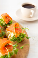 Canapes with mozzarella cheese, salad, salmon and pea sprouts, toast with red fish on a wooden board close up