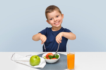A cute funny boy in a blue T-shirt eats a salad and holds a knife with a fork.