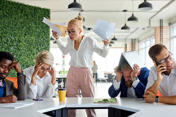 team of sad frustrated employees receiving rebuke by shouting female executive, workers are...