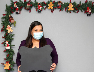 latin woman with protection mask, santa claus hat and blackboard for message.
Christmas decoration,...