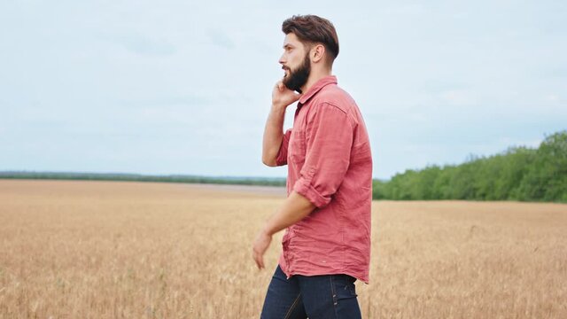 In a sunny day in the middle of large wheat field walking through the field man farmer very good looking he speaking on the phone have a concentrated discussion