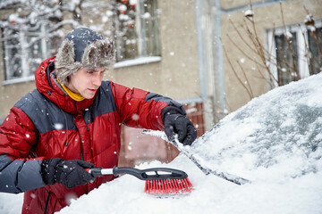 a man brushing the snow off the windshield of his car