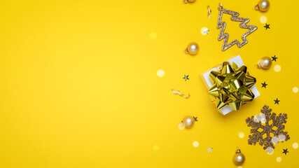 Winter banner. White gifts with golden bow, yellow balls and sparkling lights in xmas decoration on yellow background for greeting card. Flat lay, top view, copy space.