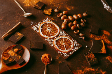 chocolate bar with orange. spices are sprinkled on the surface, orange citron and pieces of dark chocolate on a dark brown background.