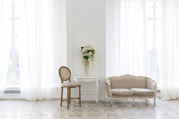 Luxury white interior of living spacious room with elegant chic furniture and high windows.