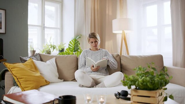 Portrait of woman relaxing with book indoors at home, mental health care concept.