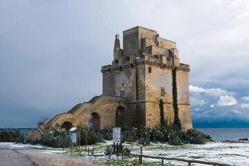 Picturesque historical fortification tower Torre Colimena in the snow on Ionian sea coast, Puglia,...