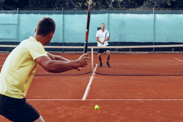 Two men playing tennis on clay tennis field