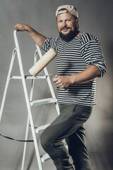 Joyful bearded craftsman with brush roller and ladder