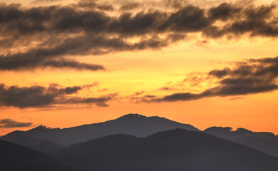 Colorful sky with clouds over the silhouettes of the hills at sunset.