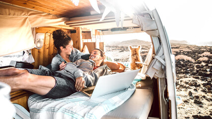 Hipster couple with dog traveling together on retro mini van transport - Digital nomad concept with indie people on minivan romantic trip working at laptop pc in relax moment - Warm contrast filter - 394780941