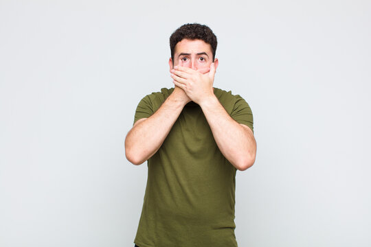 young man covering mouth with hands with a shocked, surprised expression, keeping a secret or saying oops