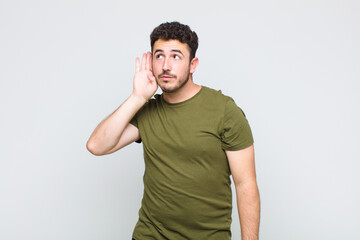 young man looking serious and curious, listening, trying to hear a secret conversation or gossip,...