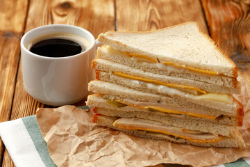 Toasted sandwich in craft paper with cup of coffee on table