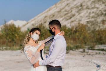 Obraz premium Young loving couple in medical masks in park during quarantine on wedding day.
