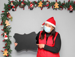 latin woman with protection mask, santa claus hat and blackboard for message.
Christmas decoration,...
