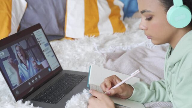African teen school girl college student distance learning on virtual distance online lesson video conference chat or watching webinar with remote teacher studying at home using laptop lying on bed.