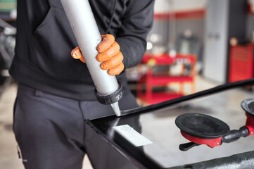 Glazier applying rubber sealing to windshield in garage, close up. High quality photo