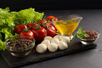 Ingredients for Italian caprese salad with mozzarella balls, tomatoes and spices, on a board