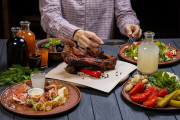 Woman with a fork and a knife in her hands begin eating set with grilled pork ribs, wine, pickled vegetables, bacon, Caesar salad , and moonshine  on black wooden background