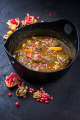 Modern style traditional Iranian fesenjan morgh stew with chicken leg and pomegranate in sour spicy sauce served as close-up in a design cast-iron roasting dish with copy space
