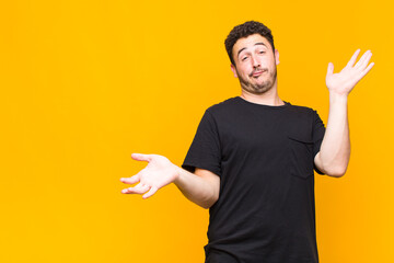 young man shrugging with a dumb, crazy, confused, puzzled expression, feeling annoyed and clueless