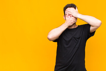 young man covering face with both hands saying no to the camera! refusing pictures or forbidding...