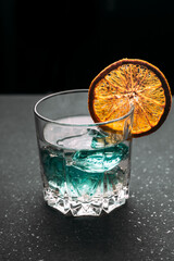 Gin in a glass with orange and ice on a black background..