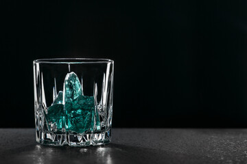 Gin in a glass on a black background with blue ice cubes on a wooden surface. Alcohol with ice. Place for an inscription..
