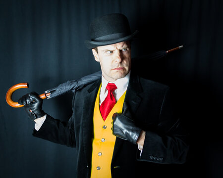 Portrait of Man in Bright Yellow Waistcoat and Bowler Hat Holding Umbrella Over His Shoulder and Scowling. Concept of Comic Book Villain or Thug