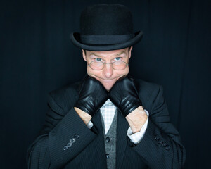 Portrait of Man in Dark Suit and Bowler Hat with Cheeks Resting on Gloved Hands. Concept of Classic and Eccentric English Gentleman. Sweet and Kind Old Man.