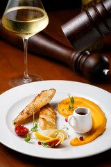 Fried fish with with berry sauce on a white plate with a glass of white wine