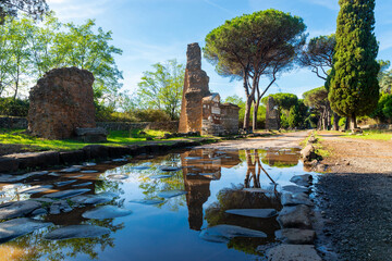 Appia Antica, Rome, reflects the remains of the tree graves in the puddle, after the storm with the blue sky and clouds, autumn day. Regina Viarum, Italy.